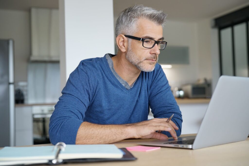 50代の副業としてAdobe Expressの無料の範囲でアイキャッチやチラシを作る、ノートパソコンで作業する中年男性のイメージ