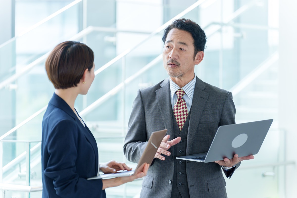 ブログ101記事のアフィリエイトリンクの点検をAIにやらせたら、145本の不備が出た 点検を仕組みにする話し合いをする、パソコンを前にしたシニアのビジネスマン二人
