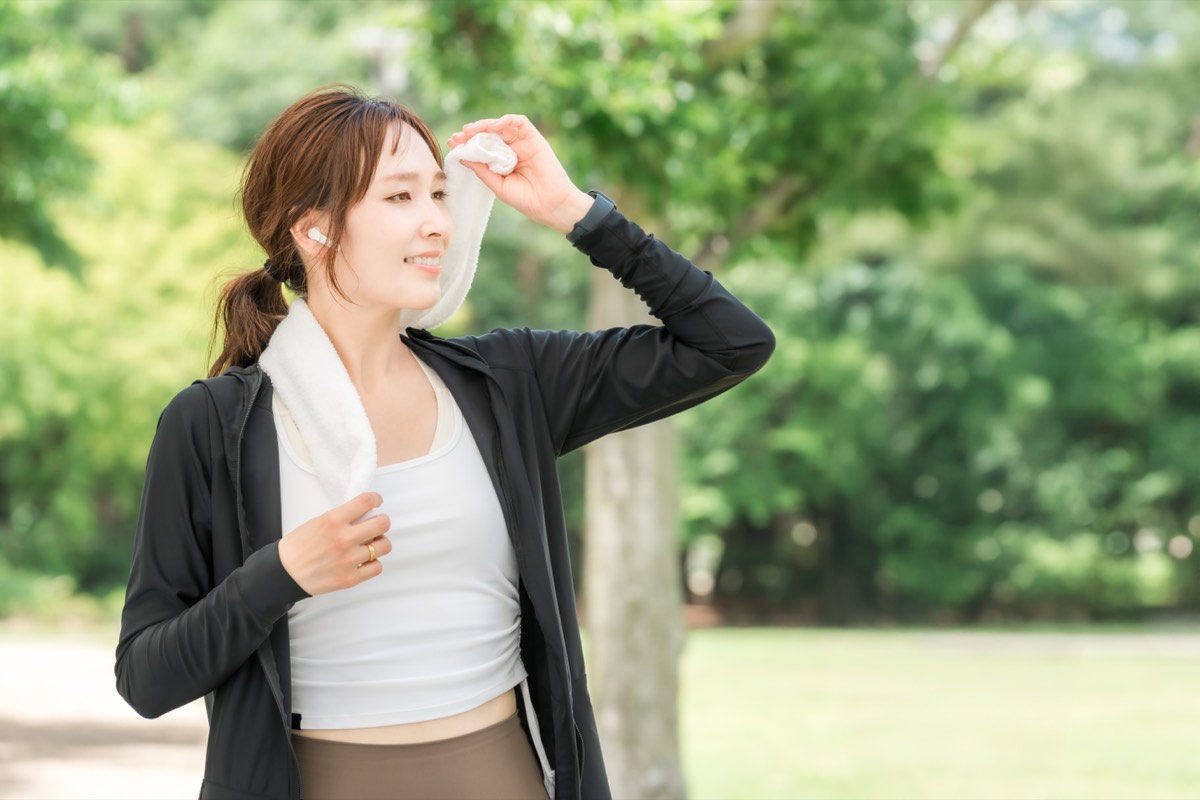公園でワイヤレスイヤホンをつけて歩く女性。耳で読む習慣のイメージ