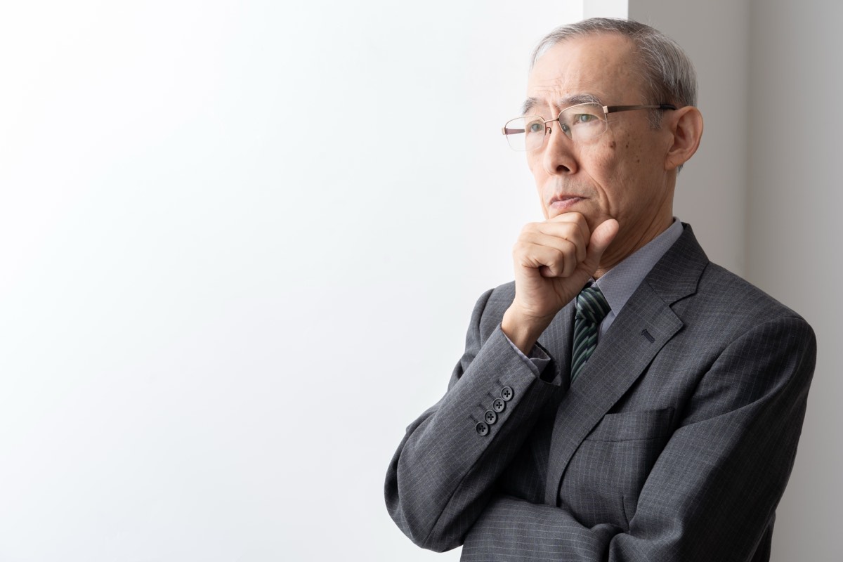 窓辺で考えごとをする50代のビジネスマン。人生の後半戦をどう生きるか
