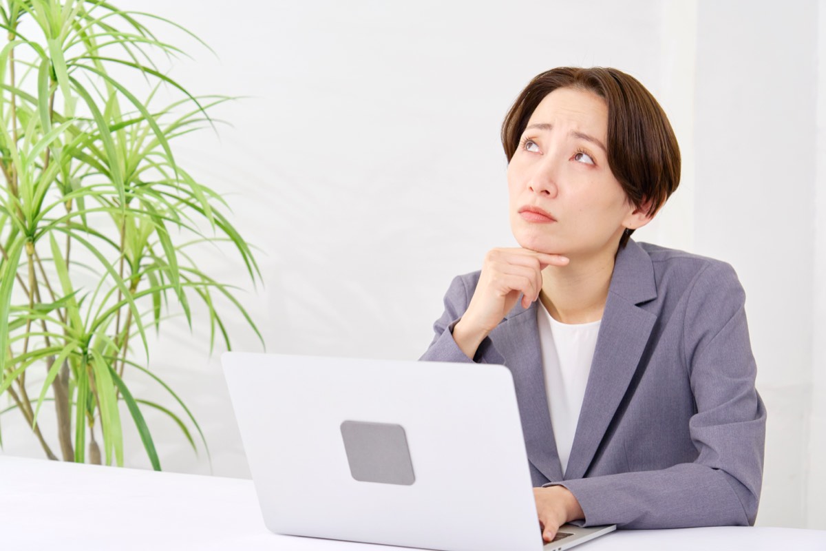 デスクで手を止めて考え込む中年の女性。判断を先送りしている状態のイメージ