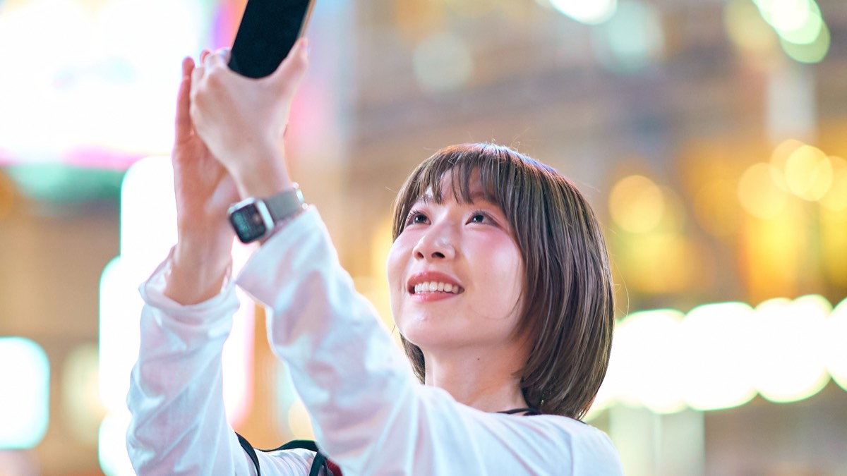 夜の繁華街でスマートフォンを掲げる若い女性