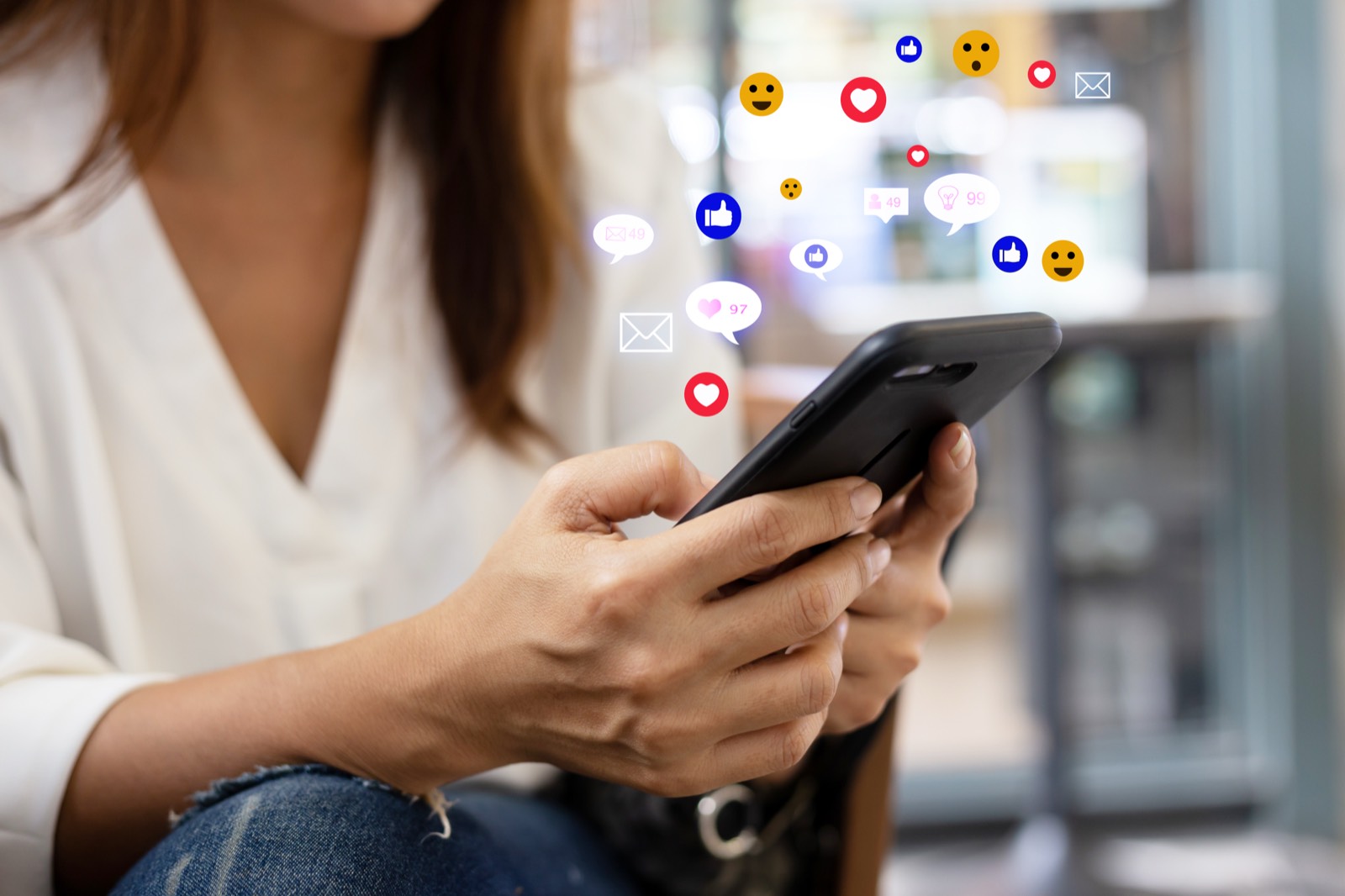 Adobe Express|デザイン経験ゼロから、今日1枚作る カフェの席でスマートフォンを操作し、投稿を確認する女性
