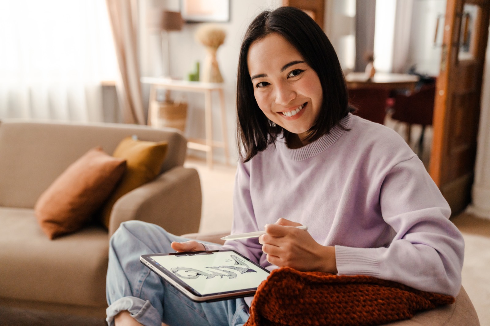 Adobe Express|デザイン経験ゼロから、今日1枚作る リビングでタブレットに向かい、笑顔でデザインを作る女性