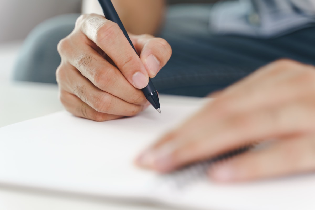 ノートにボールペンで書き込む男性の手元。あした死ぬかもよの要約の明日やる3つで、8つの質問から1つ選んで答えを1行書く場面
