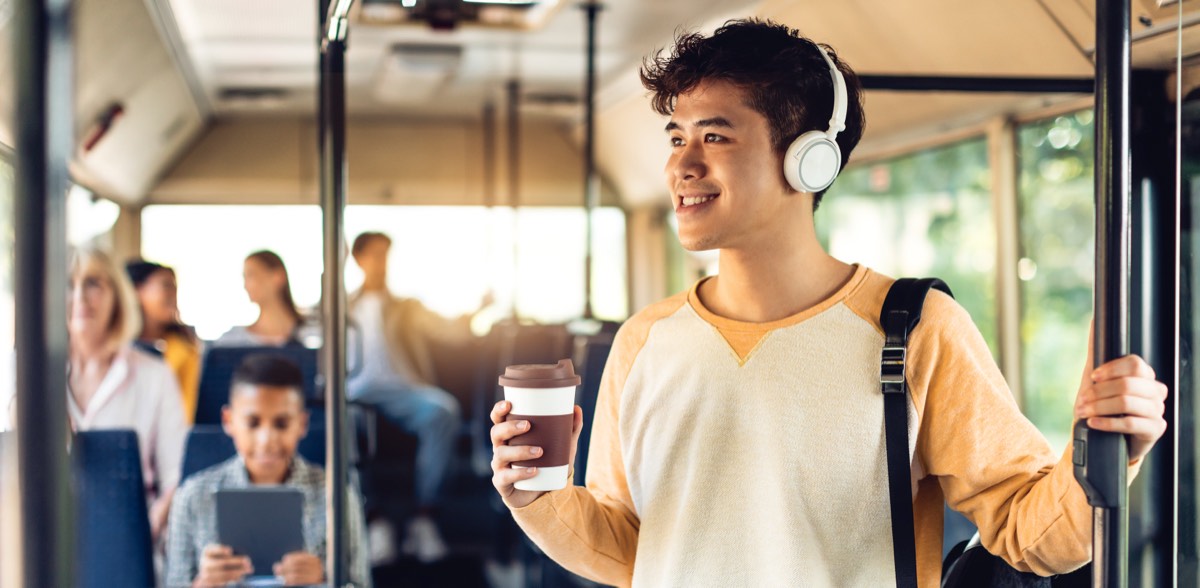 バスの座席で音楽を聴きながら笑顔で外を見るアジア系の男性。あした死ぬかもよの要約を通勤の途中でAudibleの本人朗読版で聴く場面