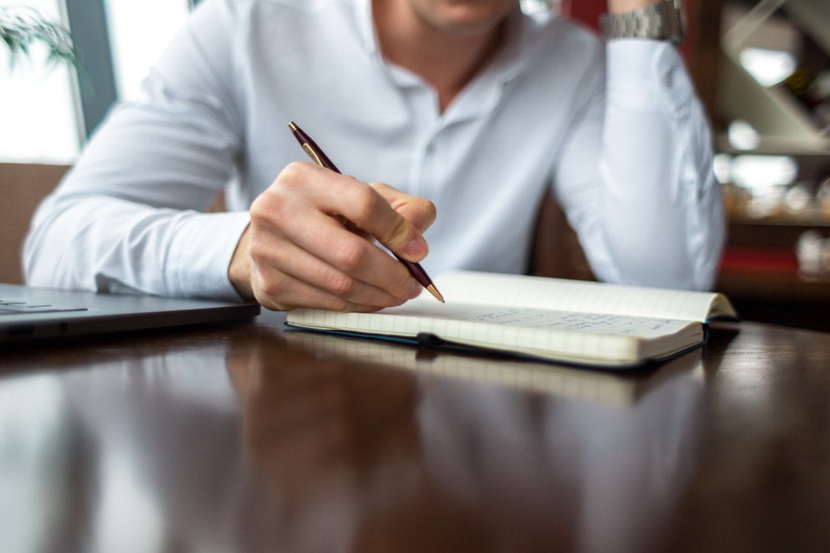 カフェでノートに1行書く男性の手元。あなた次第でこの世界は素晴らしい場所になるの要約の明日やる3つで、出来事の横に見方を1行足す場面