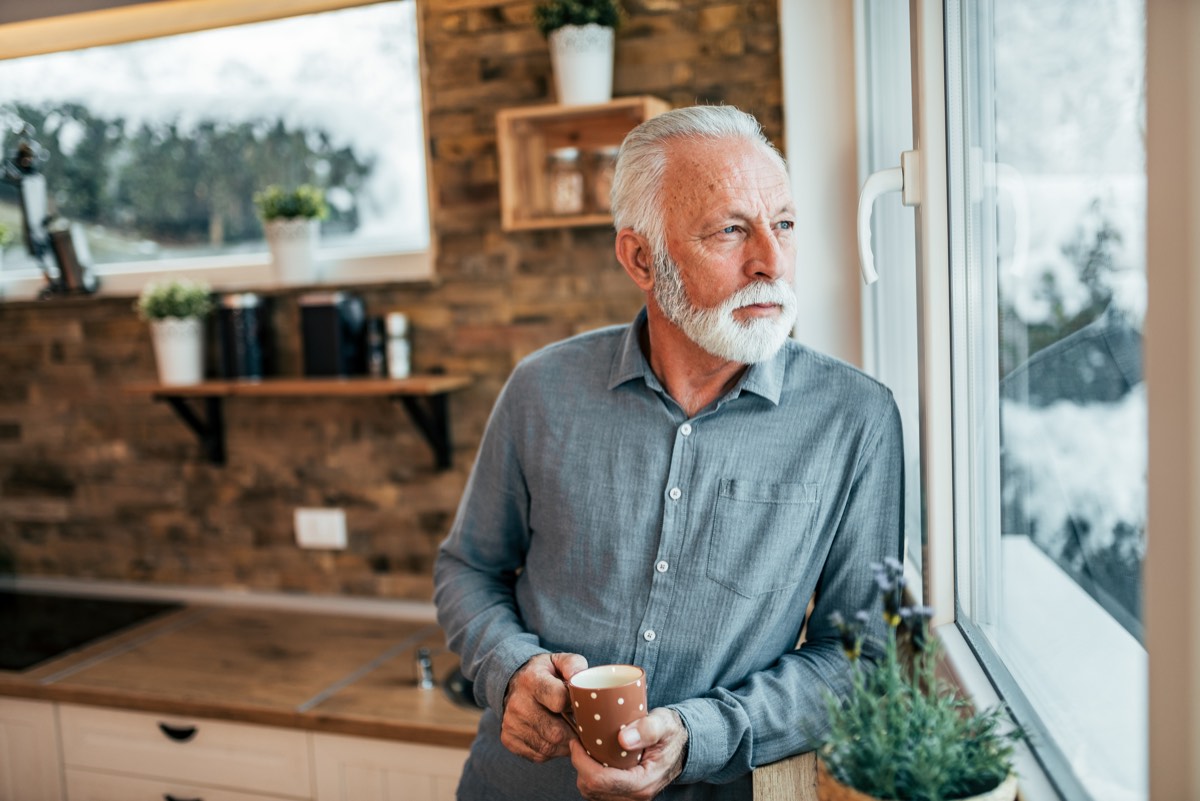 窓辺でコーヒーを飲みながら外を眺める男性。50代の燃え尽き症候群のように毎日が平坦に感じる時間