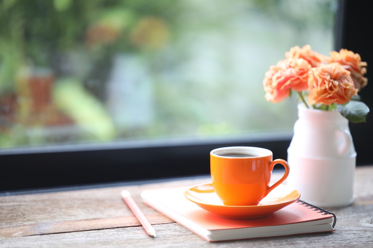 窓辺の机に置かれたノートとペンとコーヒー
