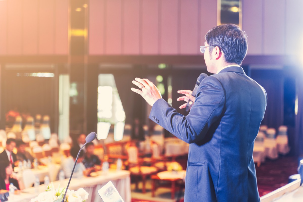会場で聴衆に向かって話す講演者。何が問題なんですかの要約で扱う質疑応答集のもとになった講演の場面
