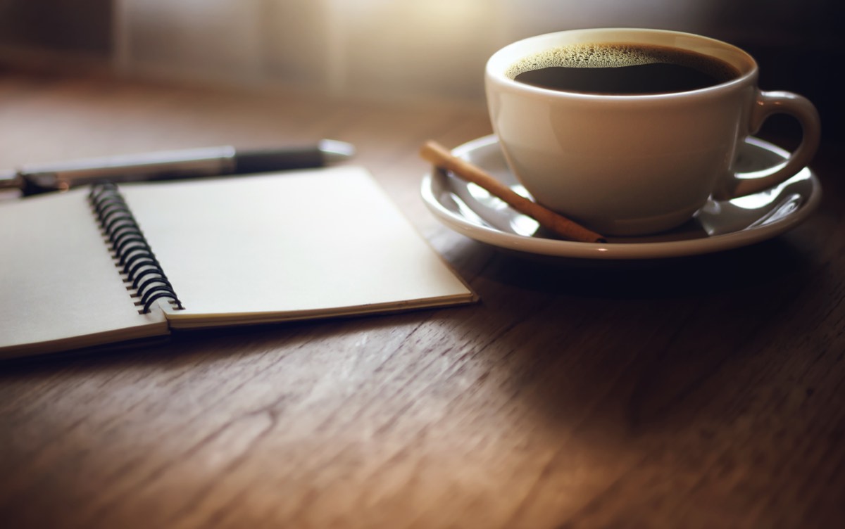 木のテーブルに置かれた開いた白紙のノートとコーヒー。開運はおうちが8割の要約の7日間の記録シートを書く場面