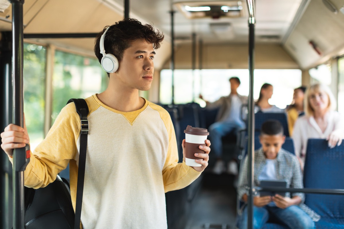 バスの中でイヤホンをしてコーヒーを持つアジア系の男性。開運はおうちが8割の要約をAudibleの朗読で通勤中に聴く場面