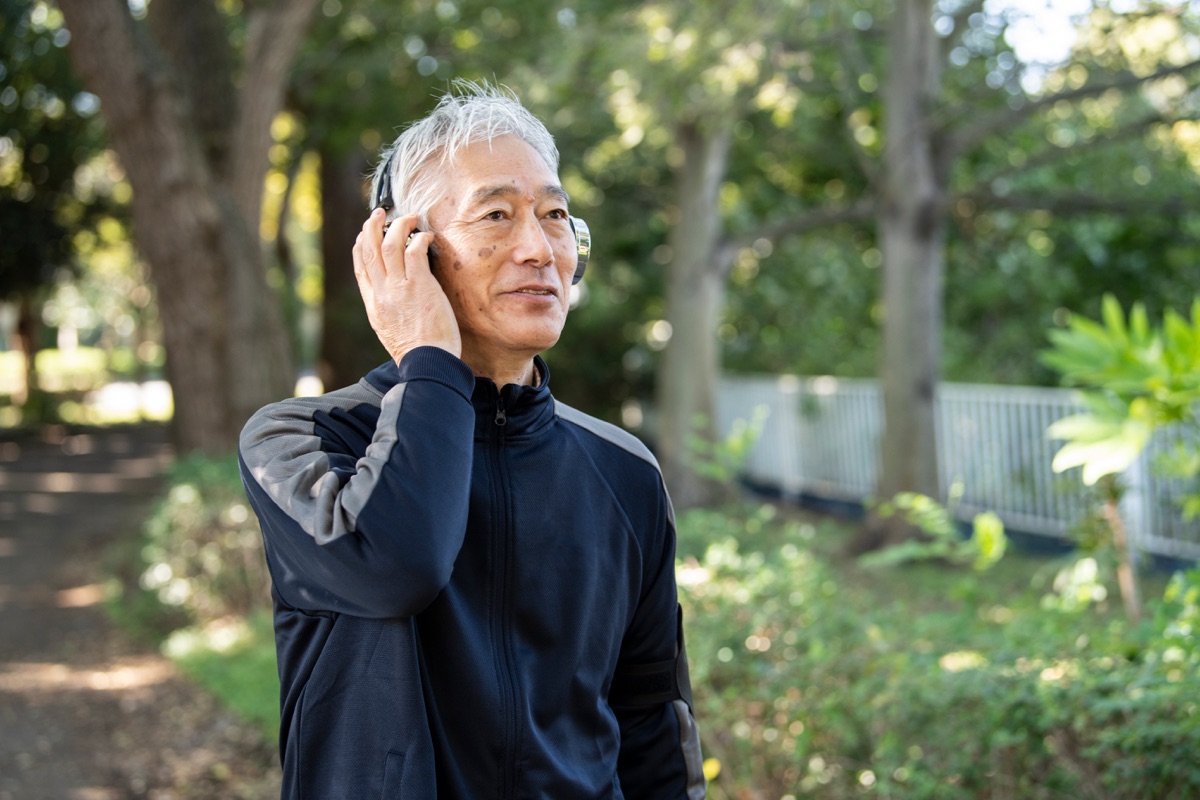 公園でヘッドホンを着けて音声を聴く高齢の男性