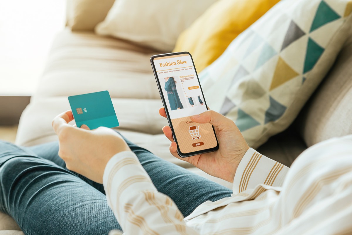 ソファでスマホとクレジットカードを持ってネットで買い物をする女性