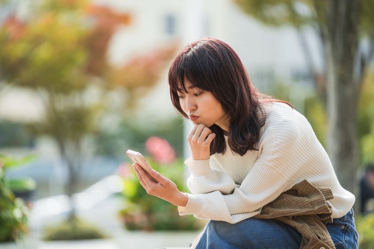 スマホの画面を見て考える女性