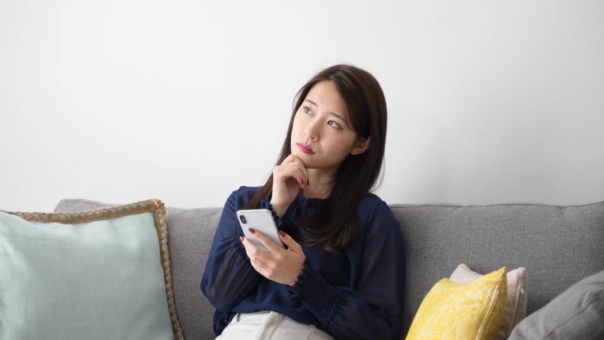 ソファでスマホを持って考える女性