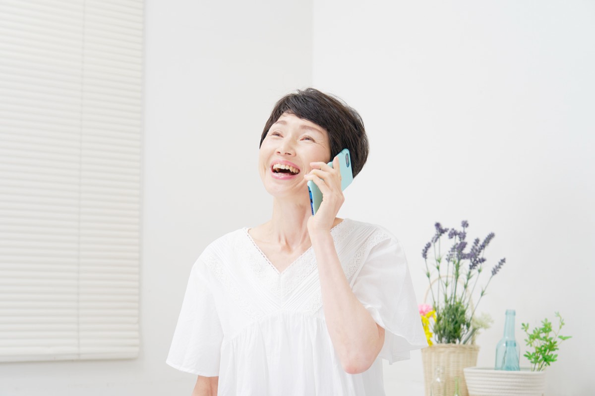リビングでスマホで電話する笑顔の女性