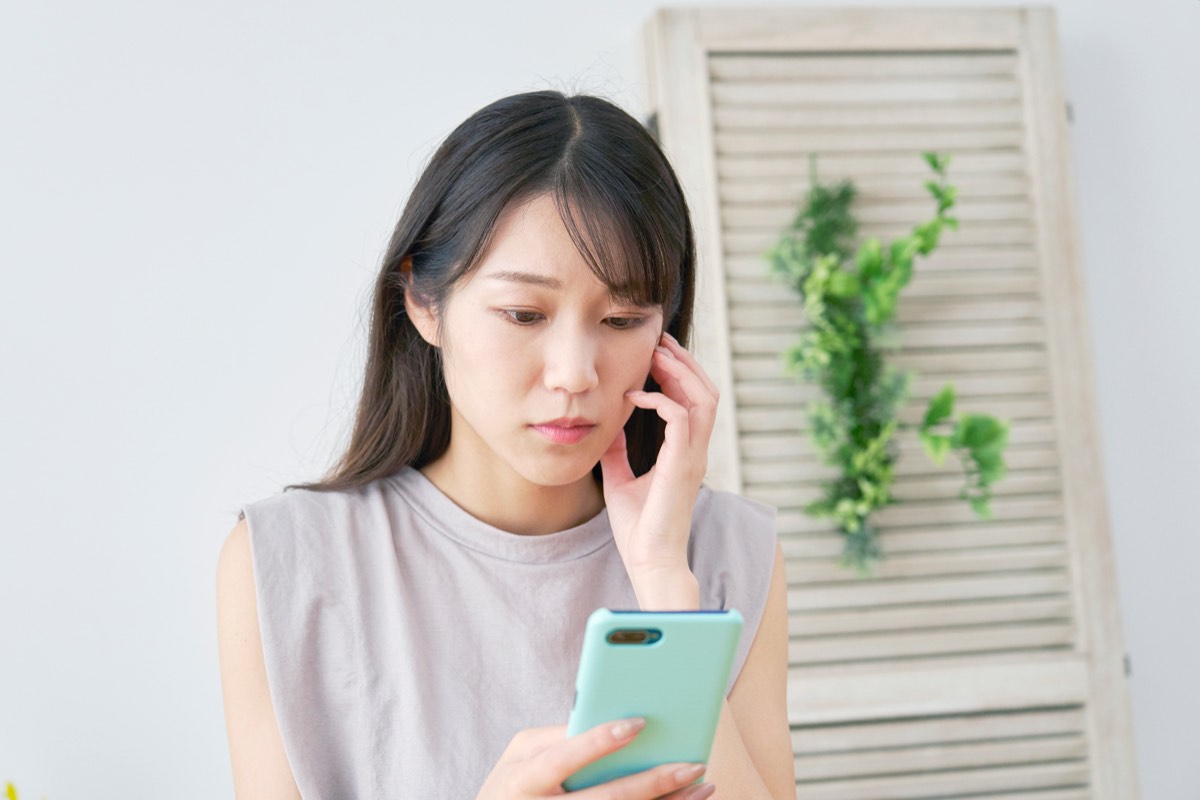 知らない番号から電話が来てスマホを持って悩む女性
