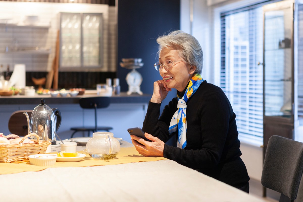 ダイニングテーブルでスマートフォンを操作するシニア女性