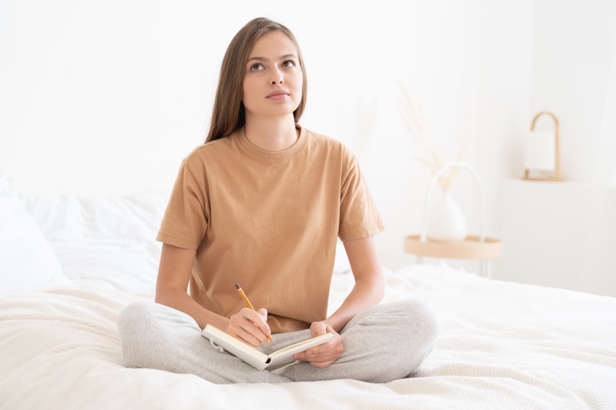 ベッドの上でノートに考えを書き出す女性。やる気が出ない日の出力の練習