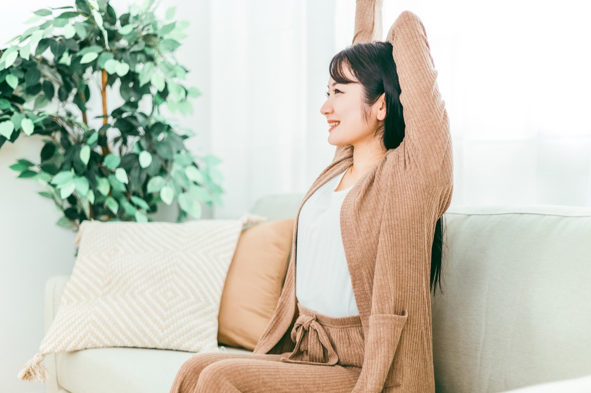 休み方がわからない人のイメージ。ソファで伸びをしてくつろぐ女性